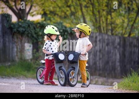 Petits enfants garçon et fille avec des casques et vélos d'équilibre en plein air jouant. Banque D'Images