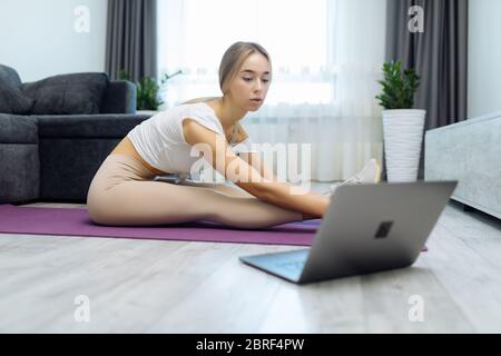 Portrait d'une jeune femme pratiquant le yoga à la maison tout en étant allongé sur un tapis avec un ordinateur portable à côté Banque D'Images