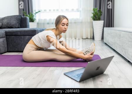 Portrait d'une jeune femme pratiquant le yoga à la maison tout en étant allongé sur un tapis avec un ordinateur portable à côté Banque D'Images