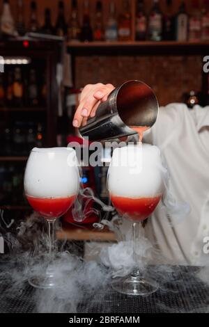 Le barman verse un cocktail rouge de l'shaker dans les verres. La fumée vient du cocktail. Banque D'Images