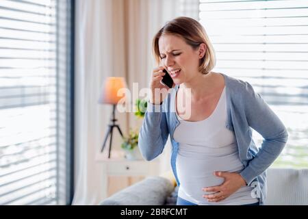 Portrait de la femme enceinte dans la douleur à l'intérieur à la maison, faisant appel d'urgence. Banque D'Images