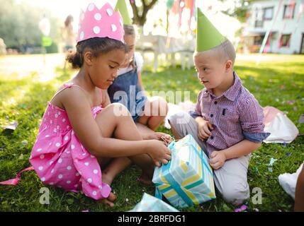 Syndrome de Down enfant avec des amis sur la fête d'anniversaire à l'extérieur, ouvrant des cadeaux. Banque D'Images