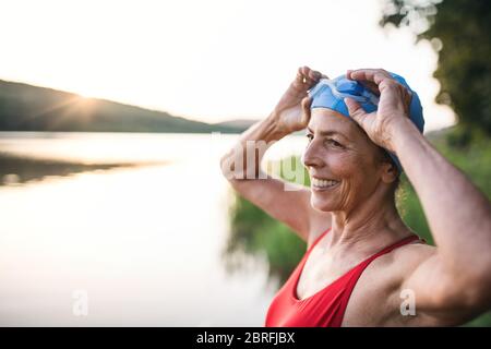 Femme âgée en maillot de bain debout près du lac à l'extérieur avant de nager. Banque D'Images