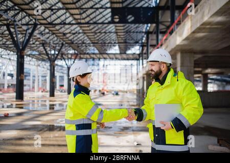 Les ingénieurs qui ont une tablette debout sur le chantier, se secouent la main. Banque D'Images