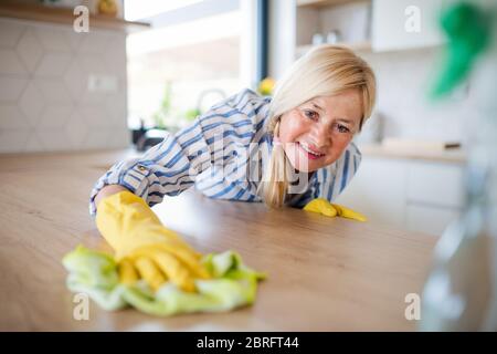 Portrait d'une femme âgée qui nettoie le comptoir de cuisine à l'intérieur à la maison. Banque D'Images