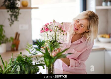 Portrait d'une femme âgée qui organise des fleurs dans un vase à l'intérieur à la maison. Banque D'Images