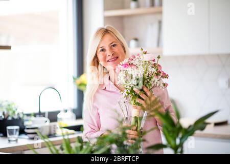 Portrait d'une femme âgée qui organise des fleurs dans un vase à l'intérieur à la maison. Banque D'Images