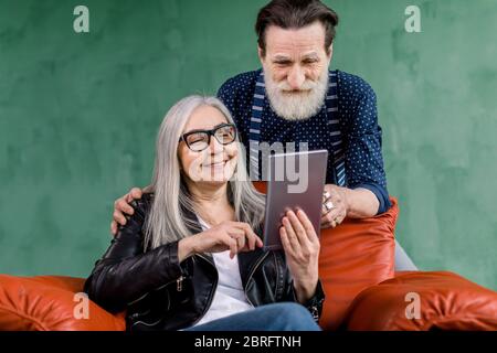 Portrait en gros plan en intérieur d'un couple de personnes âgées souriantes, d'un homme barbu et d'une femme à cheveux gris, utilisant une tablette numérique pour passer du temps ensemble Banque D'Images