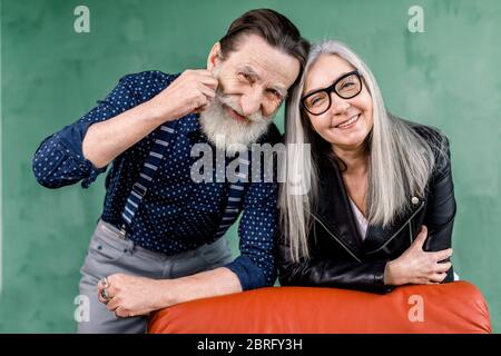 Couple âgé. Joyeux couple âgé souriant tout en étant dans une bonne humeur, se pencher sur la chaise douce rouge et toucher les fronts. Portrait romantique Banque D'Images