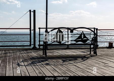 Banc en métal sur un plancher en bois devant une mer ou un lac. Banque D'Images
