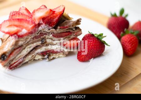 Dessert d'été léger : une tranche de gâteau en crêpe avec crème fouettée, copeaux de chocolat et fraises entre les couches. Banque D'Images