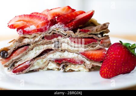 Dessert d'été léger : une tranche de gâteau en crêpe avec crème fouettée, copeaux de chocolat et fraises entre les couches. Banque D'Images