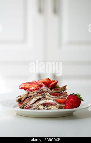 Dessert d'été léger : une tranche de gâteau en crêpe avec crème fouettée, copeaux de chocolat et fraises entre les couches. Banque D'Images