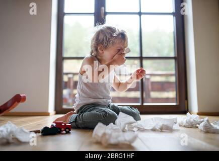 Petit garçon malade avec froid à la maison assis sur le sol, éternuant. Banque D'Images