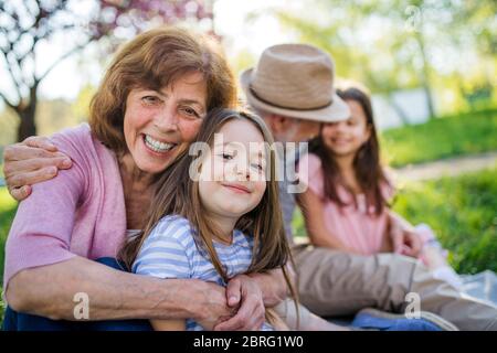 Grands-parents avec petites-filles assis dehors dans la nature printanière. Banque D'Images