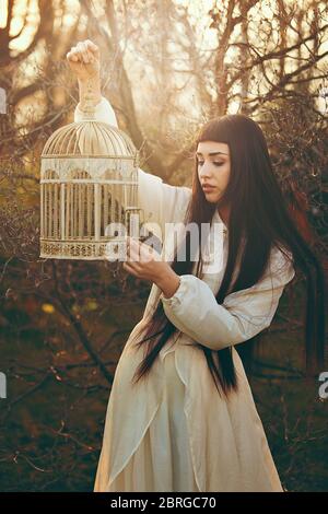 Portrait de la jeune femme au coucher du soleil avec cage d'oiseau Banque D'Images