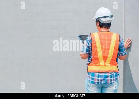 Femme d'ingénierie portant un casque blanc et tenant une tablette debout devant le mur concepts pour le contrôle et la validation de construction Banque D'Images
