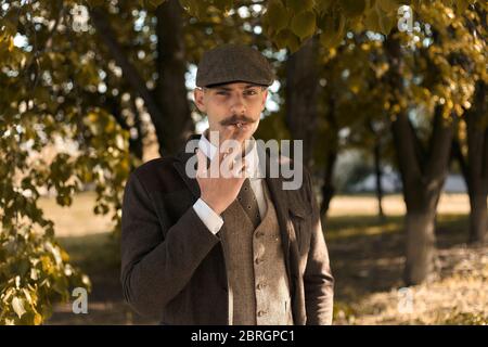 Portrait rétro des années 1920 d'un gangster anglais avec une casquette plate. Fume une cigarette dans la rue. Banque D'Images