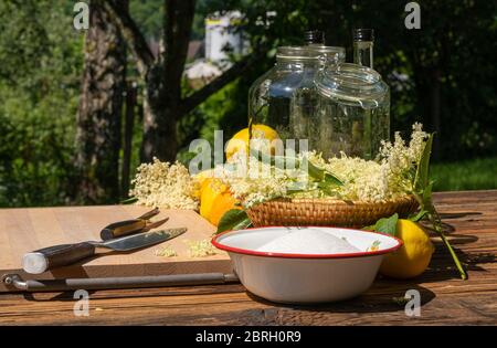 Les fleurs de sureau et autres ingrédients ainsi que les ustensiles de cuisine pour une liqueur de sureau maison sont sur une table en bois dans le jardin Banque D'Images