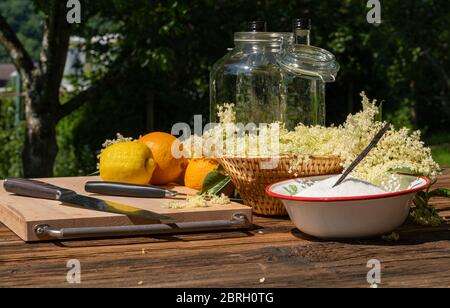 Les fleurs de sureau et autres ingrédients ainsi que les ustensiles de cuisine pour une liqueur de sureau maison sont sur une table en bois dans le jardin Banque D'Images