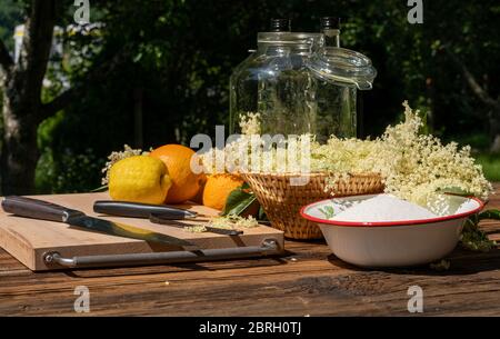 Les fleurs de sureau et autres ingrédients ainsi que les ustensiles de cuisine pour une liqueur de sureau maison sont sur une table en bois dans le jardin Banque D'Images