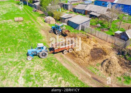 Engrais chargement de fumier pour les légumes plantés dans les champs près des bâtiments résidentiels, vue aérienne Banque D'Images