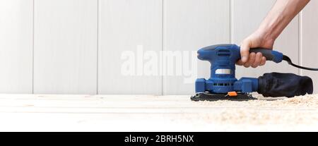 Détail de la personne travaillant avec une ponceuse électrique sur le plancher en bois naturel de sa maison. Espace pour le texte. Travail, décoration et bricolage. Banque D'Images