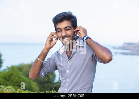 Gros plan Portrait d'un malheureux beau jeune homme en chemise bleue faisant face drôle ayant la douleur dans les oreilles en raison de la musique forte que l'écoute removi Banque D'Images