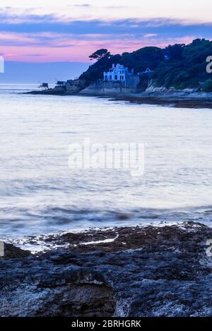 Saint-Palais-sur-Mer, France : cabanes traditionnelles de pêche et luxueuse villa avec vue sur la mer, bâtie sur la côte près du centre ville, au coucher du soleil. Banque D'Images