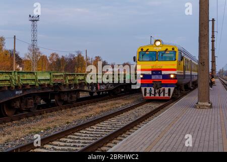 Train de banlieue arrivant à la plate-forme de la gare dans la soirée. Façade jaune-bleu du train à la gare de Riga. Transport Co Banque D'Images