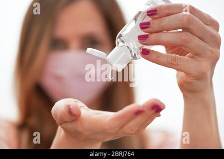 Jeune femme avec du coton rose fait maison bouche visage virus masque compte-gouttes anti bactérien alcool gel à frotter sur la main, détail à la bouteille blanche, visage flou Banque D'Images