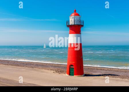 Voilier passant le phare à Westkapelle, province de Zeeland, pays-Bas. Westkapelle est une petite ville d'environ 2,600 habitants. Banque D'Images