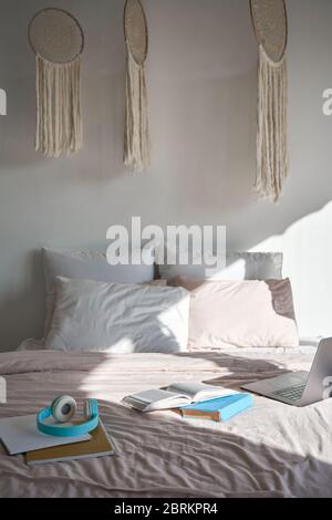 Chambre moderne avec ordinateur portable, casque, livres sur un lit confortable, verticale. Banque D'Images