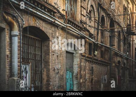 Façade abîmé d'une ancienne usine de textile abandonnée avec portes, fenêtres, tuyaux et câbles Banque D'Images