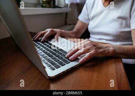 Gros plan sur les mains de femme âgée qui tapent sur un ordinateur portable. Une vieille femme écrit la main sur un ordinateur portable à la maison. Banque D'Images