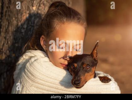 une jeune fille adorée épouse son chien bien-aimé et s'assoit à la lumière du coucher de soleil à l'extérieur de la nature Banque D'Images