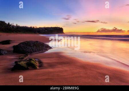 Sable lisse des plages du nord de Sydney au lever du soleil face aux vagues floues de l'océan Pacifique. Banque D'Images