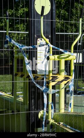 Équipement de gym extérieur dans le parc, enveloppé dans des bandes de danger et de police, puis enroulé derrière des écrans de mesh pendant le confinement pandémique COVID-19. Banque D'Images