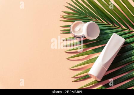 Produits naturels de beauté biologique pour la peau. Emballage vierge sans marque pour pot et tube crème sur feuille de palmier verte. Arrière-plan jaune, vue de dessus, plat, copie Banque D'Images