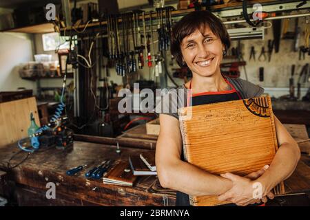 Une artiste féminine tient son œuvre d'art en bois et sourit un atelier Banque D'Images