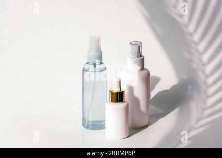 Tonique cosmétique, sérum et eau micellaire en paquets vierges sur un fond de mur blanc avec ombre des feuilles de palmier. Concept de produits naturels pour la peau. Banque D'Images