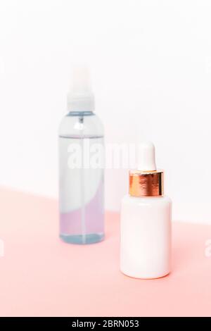 Deux flacons avec sérum et lotion cosmétique sur table rose contre paroi blanche. Emballages vierges sans marque. Concept de produits naturels pour la peau. Banque D'Images