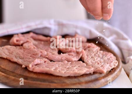 Homme cuisant des steaks de viande dans la cuisine. Chef salant et poivrant la viande sur fond de bois Banque D'Images