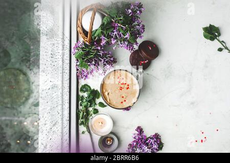 café dalgona avec mousse, biscuits au chocolat, bougies allumées et fleurs fraîches et luxuriantes de lilas pourpres à la fenêtre humide avec gouttes et gouttes de la pluie. Banque D'Images