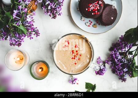 café de dalgona avec mousse et copeaux de chocolat sous forme de coeurs, biscuits au chocolat, bougies en feu et fleurs fraîches et luxuriantes de lilas pourpres sur une lumière Banque D'Images