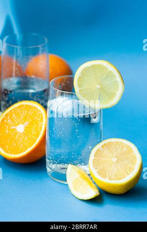 deux verres d'eau claire étincelante avec des bulles et des agrumes mûrs et des agrumes des oranges de citron dans une coupe et entières sur fond bleu. prenez vita Banque D'Images