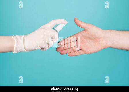 Arrêter la propagation du coronavirus patient concept. Photo courte en gros plan de la femme en gants vaporise de l'assainisseur sur la main de l'homme isolé sur bleu turquoise b Banque D'Images
