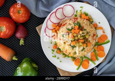Plat avec riz et légumes, décoré de tranches de carottes et de radis et de bandes de piment. D'un côté de l'assiette il y a deux tomates, une carotte et Banque D'Images