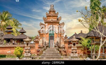 Vue sur la rue d'un temple hindou balinais près d'Ubud, avec une porte en briques rouges et un mur extérieur, et des toits de chaume de pavillons intérieurs. Banque D'Images