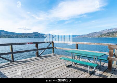 Table de pique-nique sur le quai de Naramata avec vue panoramique sur le lac Okanagan, les montagnes et le ciel bleu Banque D'Images